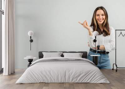 A radiant young woman with brown hair and a white blouse gestures with one hand Wall mural