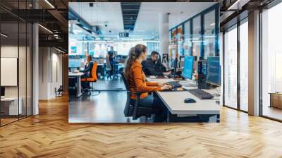 A woman in an orange shirt sits at a desk in an open office setting, typing on a computer keyboard. Other people are working in the background. Wall mural