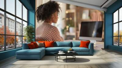 A woman is seated at a desk, focused on her computer screen as she works. Wall mural