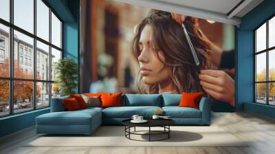 A woman sits in a salon chair while a stylist cuts her hair. The woman is looking down and the stylist is using a comb to style her hair. Wall mural