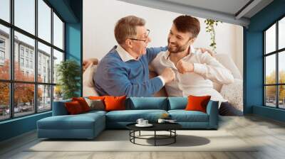 Adult Son And Elderly Father Bumping Fists Sitting On Couch At Home. Relationship With Senior Parents. Selective Focus Wall mural