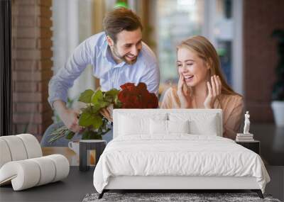 Affectionate millennial man surprising his girlfriend, giving her bouquet of flowers in cafe Wall mural