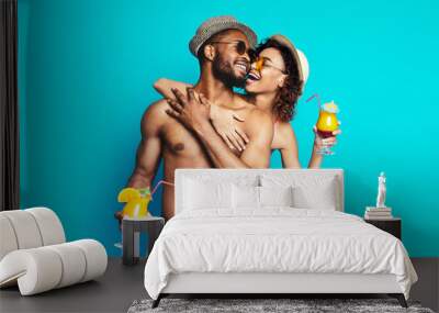 African American happy couple, both wearing sunglasses and summer clothing, smiles and laughs while holding refreshing cocktails Wall mural