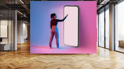 African american lady touching screen of giant smartphone in neon light, mockup for mobile app or website design Wall mural