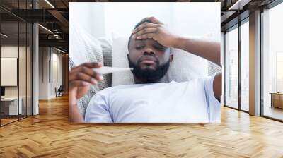 African-american man checking his body temperature at home Wall mural