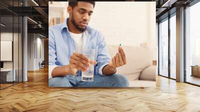 African-american man holding glass of water and looking at pill Wall mural