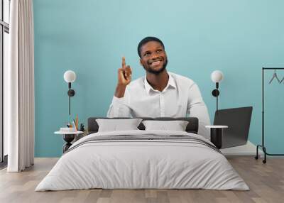 African american office worker having creative idea, gesturing eureka while sitting at workplace on blue background Wall mural