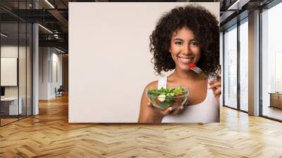 African-american woman eating vegetable salad over light background Wall mural