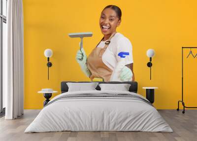 African housekeeper woman holding spray and squeegee over yellow background Wall mural