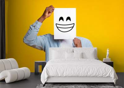 African man hiding face behind paper with drawn happy emoticon Wall mural