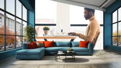 Afro businessman working on laptop in modern office, side view Wall mural