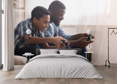 Afro father and son playing video games with joysticks Wall mural