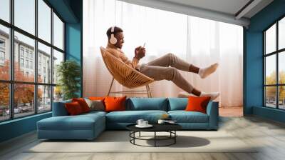 Afro Guy In Headphones Using Smartphone Sitting On Chair Indoor Wall mural