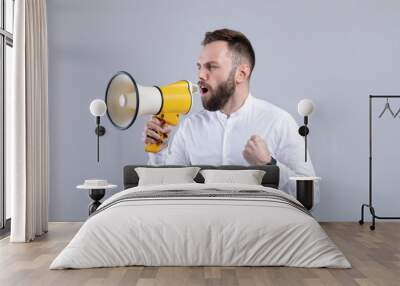 Agitated young man screaming into megaphone on grey studio background Wall mural