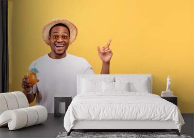 Amazing offer. Excited African American man with yummy summer cocktail pointing at blank space on yellow background Wall mural