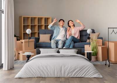 Asian couple planning home renovation amid boxes on sofa indoor Wall mural