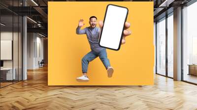 Asian man holding large cellphone blank screen leaping in studio Wall mural