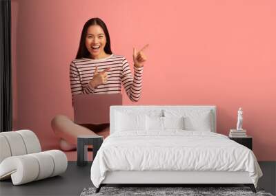 Asian woman sitting on floor with laptop and pointing at copy space Wall mural