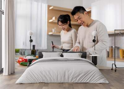 Attractive korean man and woman cooking together at home Wall mural