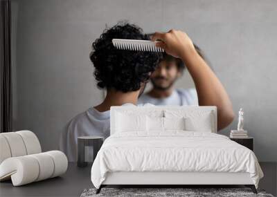 Back view of indian curly man combing hair standing near mirror in bathroom. Male haircare routine concept Wall mural