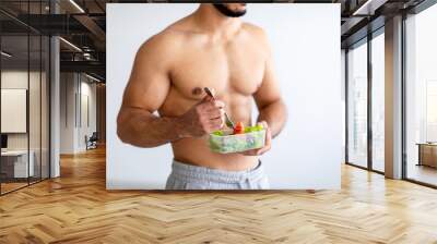 Balanced diet concept. Cropped view of strong young man with bare torso eating vegetable salad at home Wall mural