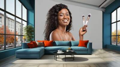 Beautiful black woman holding makeup brushes and smiling to camera Wall mural