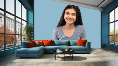 Beautiful Indian teenage girl with dark long hair smiling and looking at camera on blue studio background Wall mural