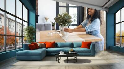 beautiful young brunette woman arranging plants in vase, decorating dining room table, creating cozy Wall mural