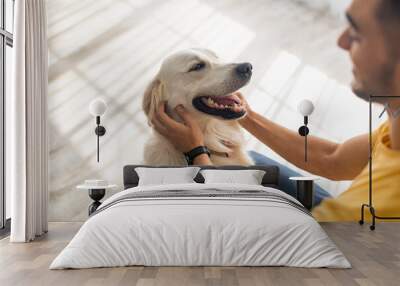 Best friend concept. Millennial Arab man scratching his dog on floor at home, selective focus Wall mural