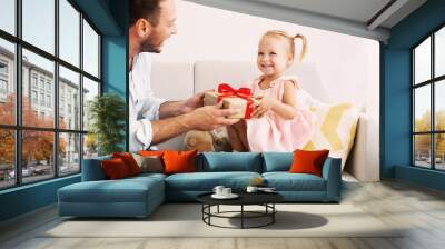 Birthday Present. Happy loving family sitting on the couch and holding gift box with red bow Wall mural