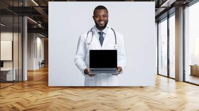 Black cheerful doc in white robe holding blank laptop screen Wall mural