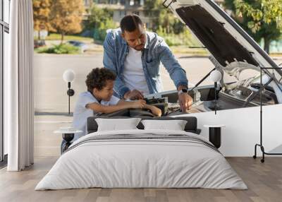 Black father and preteen son checking car engine outdoors Wall mural