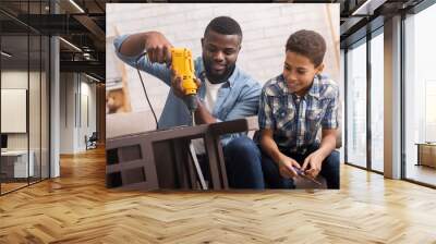 Black father teaching his son how to use drill perforator Wall mural