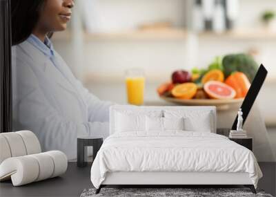 Black female dietitian with laptop consulting patient online at clinic, sitting at desk, side view, cropped Wall mural