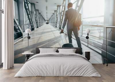 Black man professional is walking with his luggage near an airport. The environment is contemporary and bustling, capturing the essence of a busy business traveler's routine, back view Wall mural