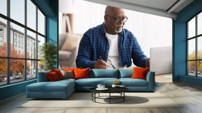 Black Man Using Laptop Taking Notes In Office, Wearing Eyeglasses Wall mural