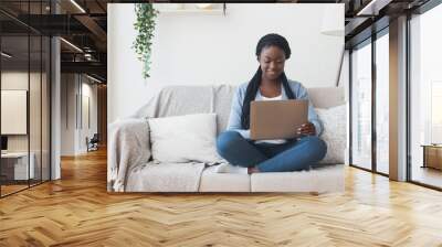 Black millennial woman working with laptop computer on sofa at home Wall mural