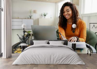 Black woman sitting at desk, using pc writing in notebook Wall mural