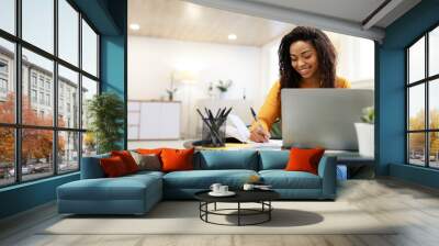 Black woman sitting at desk, using pc writing in notebook Wall mural