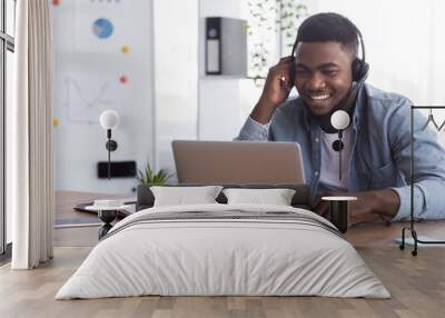 Black worker wearing headphones, watching webinar on laptop in office Wall mural