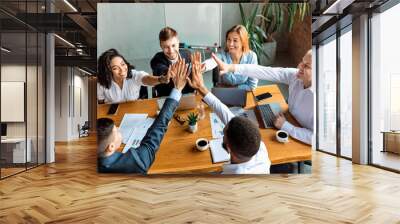 Business Team Giving High-Five Sitting At Table In Modern Office Wall mural