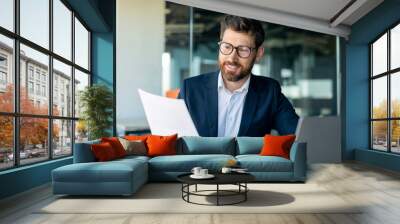 Busy middle aged businessman working with laptop and documents, sitting at desk in office, checking financial reports Wall mural