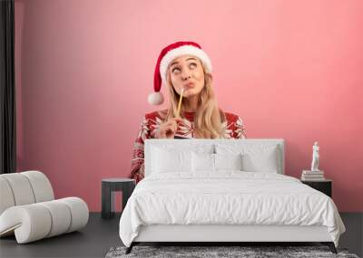 Charming young lady in Christmas outfit thinking about her New Year resolutions, writing wish list over pink background Wall mural