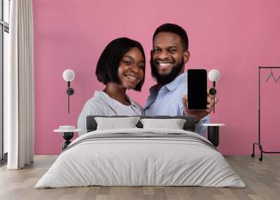 Check this app. Romantic black couple showing smartphone with blank screen over pink background, mockup for design Wall mural