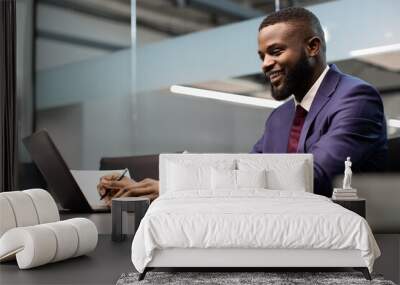 Cheerful african american entrepreneur signing papers, working on laptop Wall mural