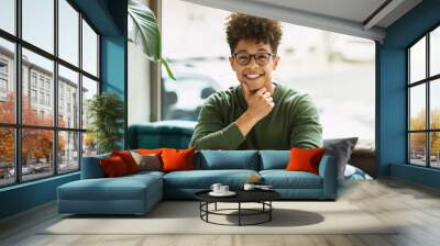 Cheerful african american guy sitting at table next to window Wall mural