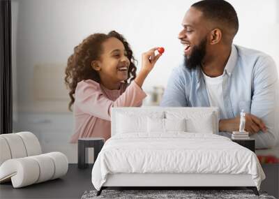 Cheerful african daughter cooking fresh salad feeding dad Wall mural