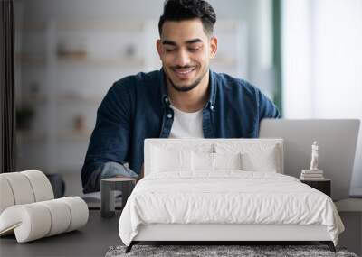 Cheerful arab guy using smartphone while sitting at workdesk Wall mural