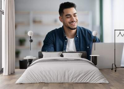 Cheerful arab guy working on laptop, taking notes Wall mural