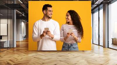 Cheerful Arab Man And Woman Holding Smartphones And Looking At Each Other Wall mural